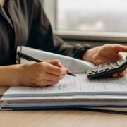 Person calculating finances with a calculator and writing in a notebook.